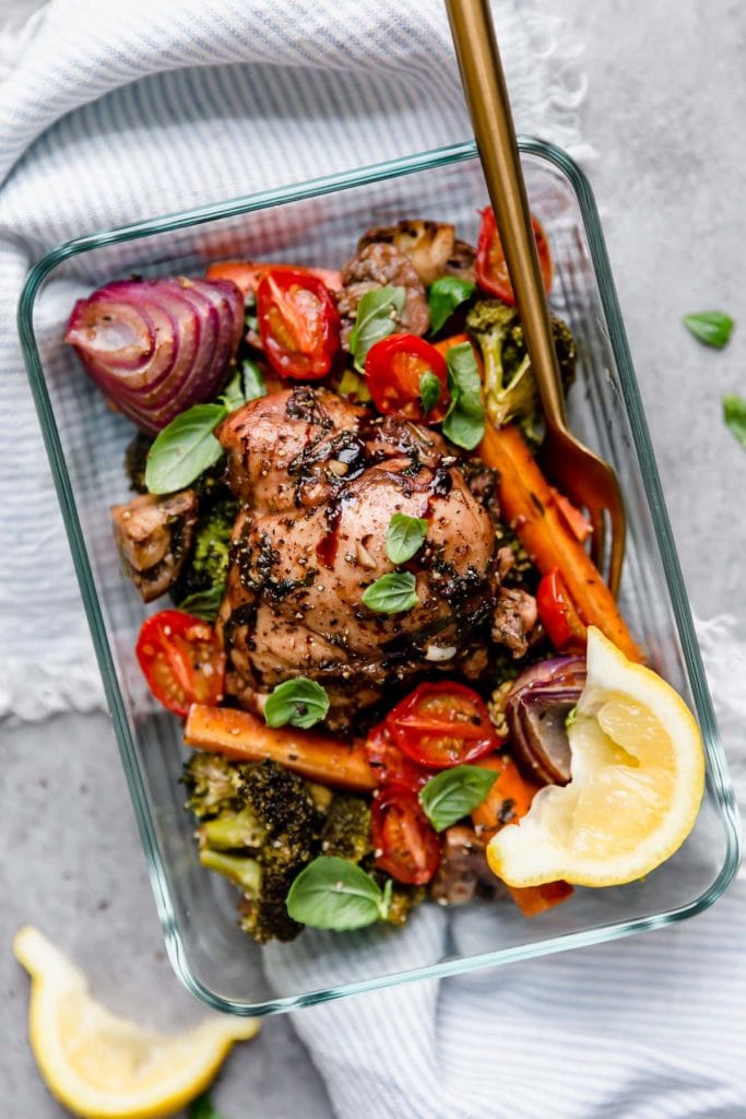 Meal prep container with serving of sheet pan balsamic chicken and veggies, gold cutlery on side