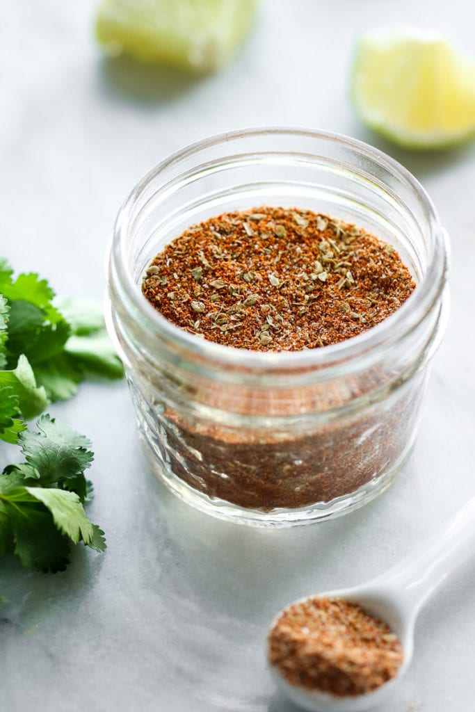 Homemade taco seasoning in a small mason jar with fresh cilantro and lime in the background