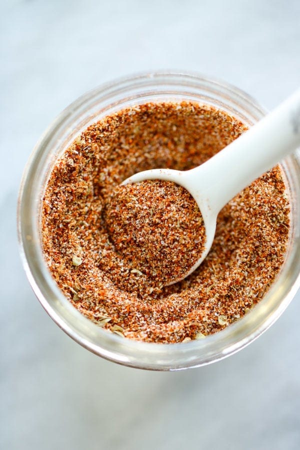 Close up view of homemade taco seasoning in a small jar with a white teaspoon in it