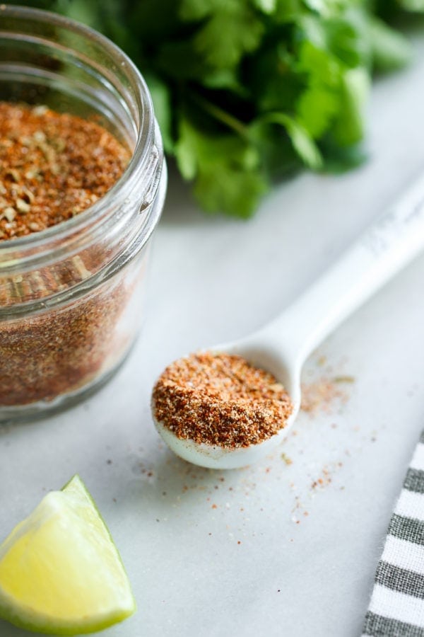Homemade taco seasoning in a white teaspoon next to a jar filled with taco seasoning