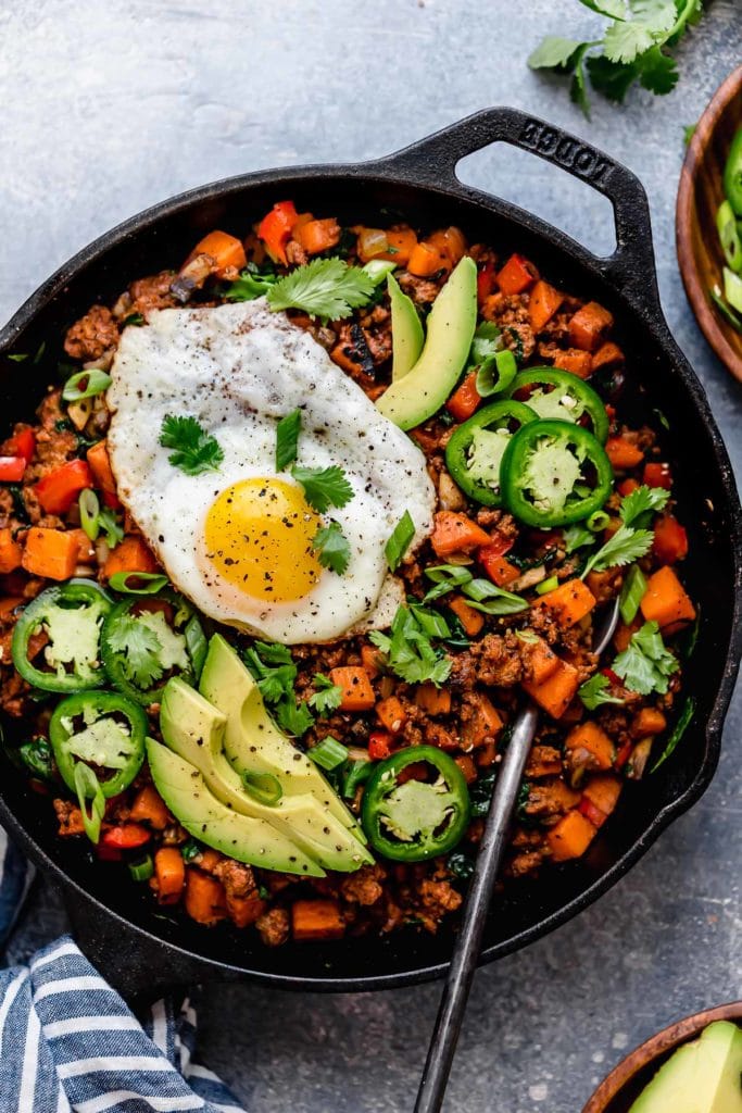 Tex-Mex Sweet Potato Hash in a cast iron skillet topped with a fried egg and avocado slices.