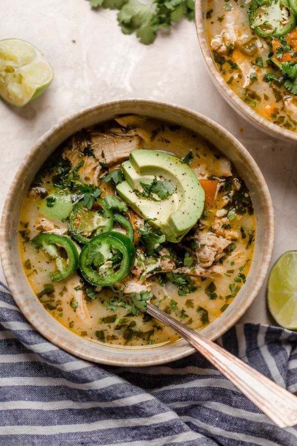 Stone bowl filled with slow cooker white chicken chili topped with avocado slices and jalapeño slices.