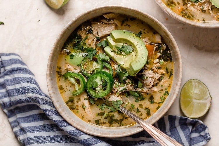 An overhead view of slow cooker white chicken chili in a cream bowl and topped with jalapeno and avocado slices