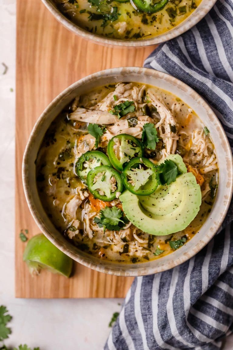 overhead image of a bowl of white chicken chili topped with avocado and jalapeño slices