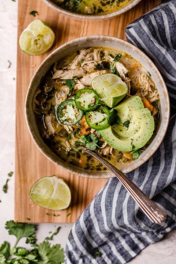 Bowl of white chicken chili with spoon garnished with jalapeños, avocado and limes on wooden cutting board. This recipe ranked #1 of the Most Popular Recipes of 2019.