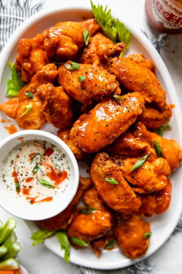 A white serving platter piled high with crispy baked buffalo wings and a side of homemade ranch dressing