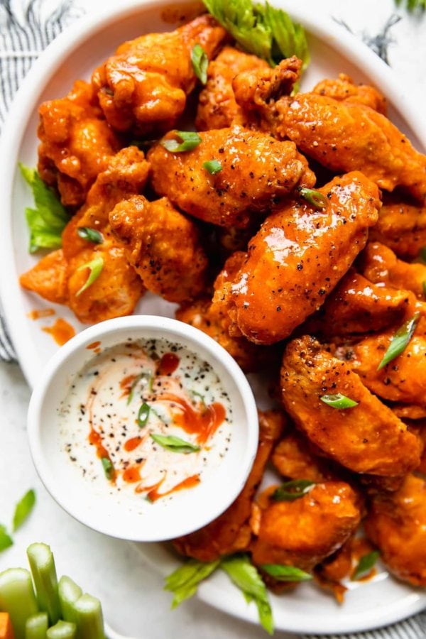 A white platter topped high with crispy baked Buffalo wings and a side of homemade ranch dressing