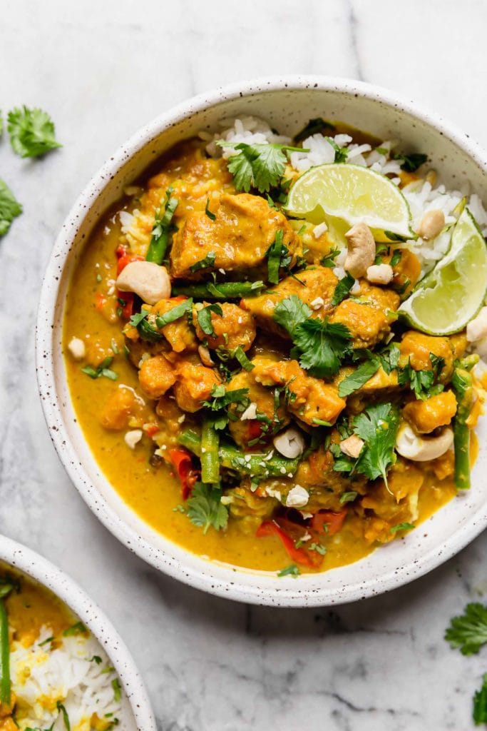 Instant Pot Chicken Sweet Potato Curry served over white rice in a white speckled bowl garnished with cilantro, lime wedges and cashews.