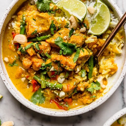 Overhead view of chicken sweet potato curry garnished with fresh cilantro and cashews in a speckled bowl