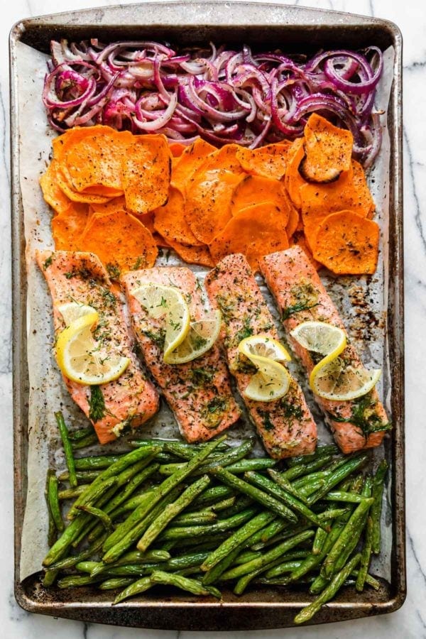 Lined up on a baking sheet, green beans, salmon fillets, sweet potato rounds, and purple onion.