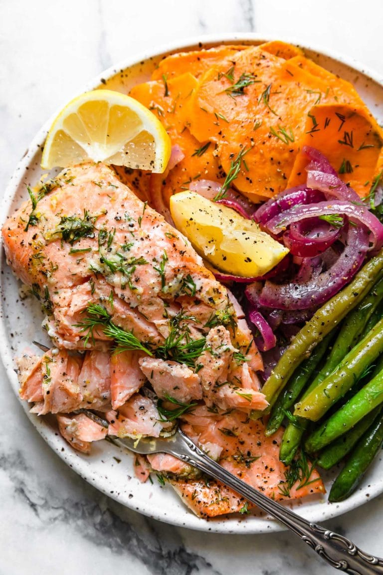 Overhead view of a plate of sheet pan baked salmon with colorful vegetables garnished with lemon wedges. 