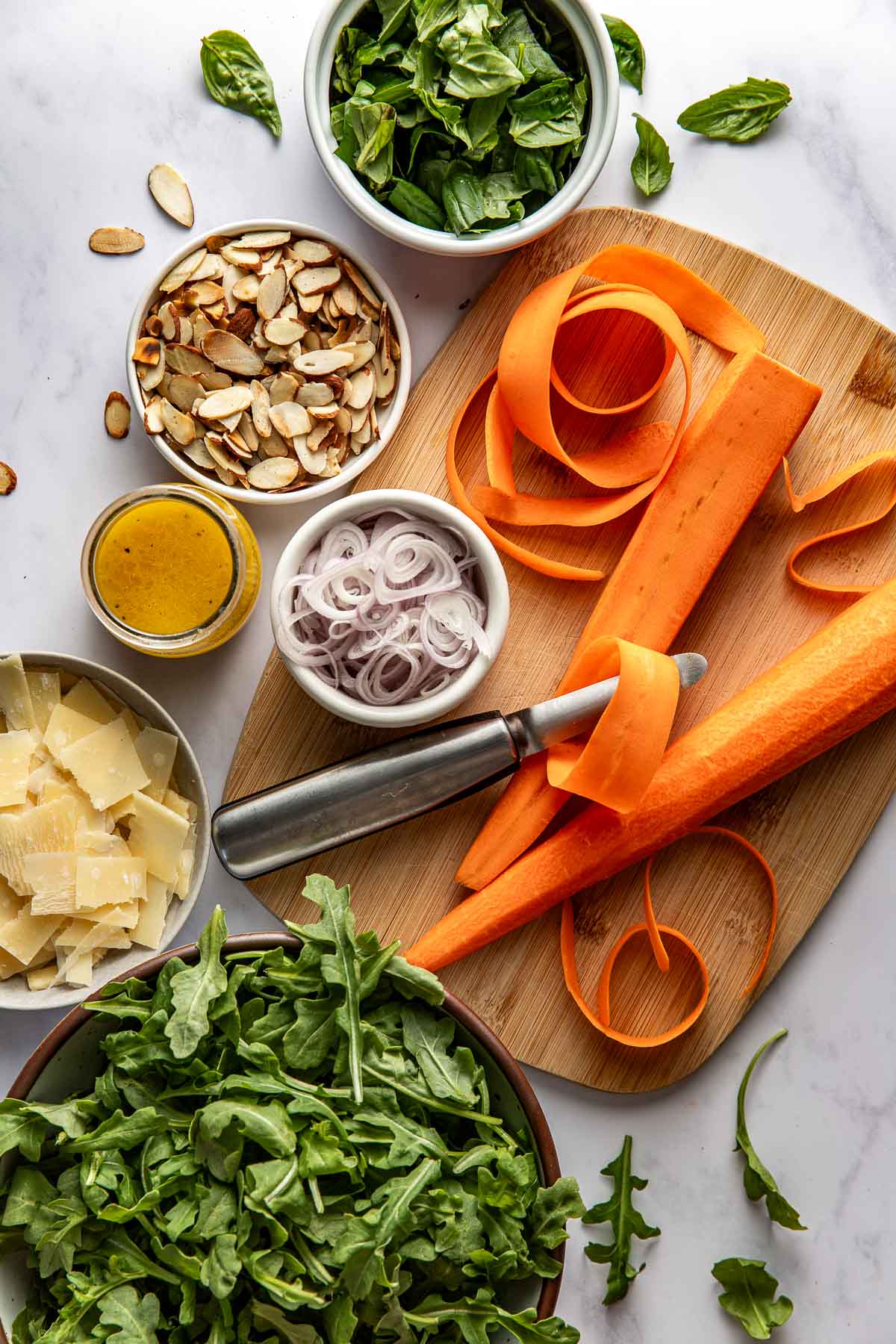 Overhead view of Arugula Salad ingredients on a wood cutting board and in bowls surrounding it. 