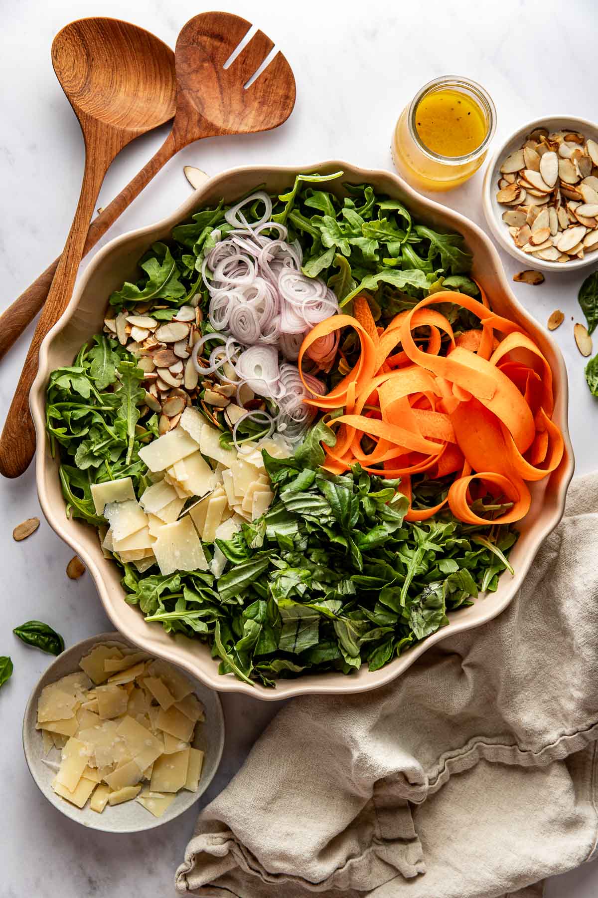 An arugula salad with almonds, shallots, ribboned carrots, and Parmesan in a bowl.