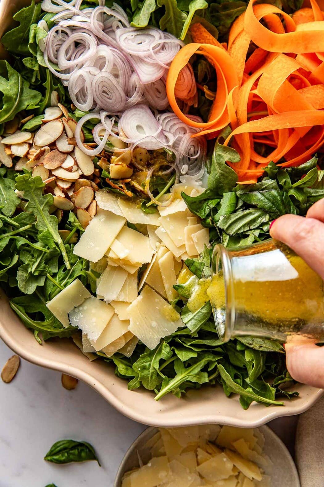 Overhead view of a hand pouring vinaigrette over an Arugula Salad with Lemon, Basil, and shaved parmesan cheese