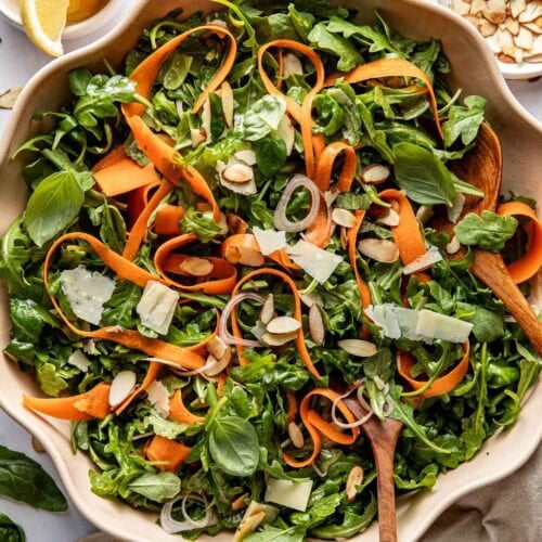 Overhead view of a colorful bowl of Arugula Salad With Lemon And Basil topped with shaved parmesan cheese.