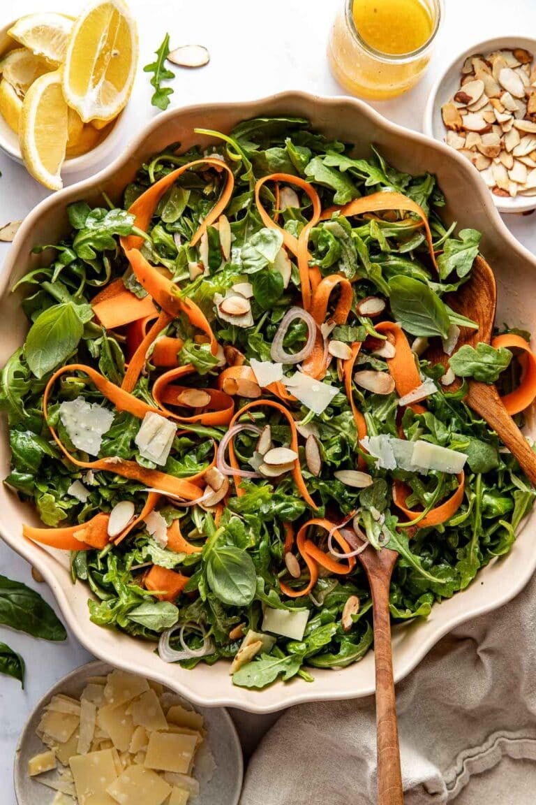 Overhead view of a bowl filled with arugula and carrot ribbons topped with almonds, onions, and shaved parmesan. 