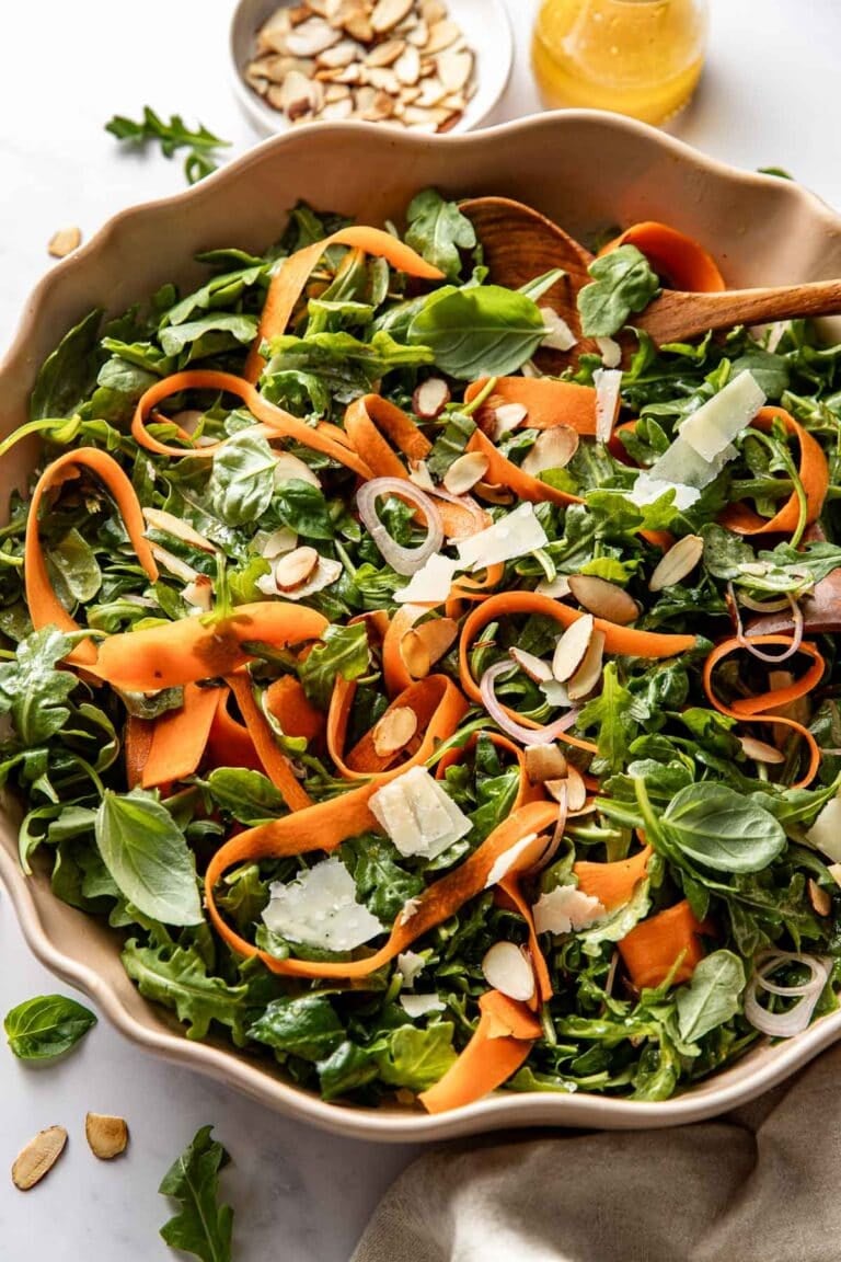 Overhead view of a serving bowl of arugula salad with lemon and basil topped with slivered almonds.