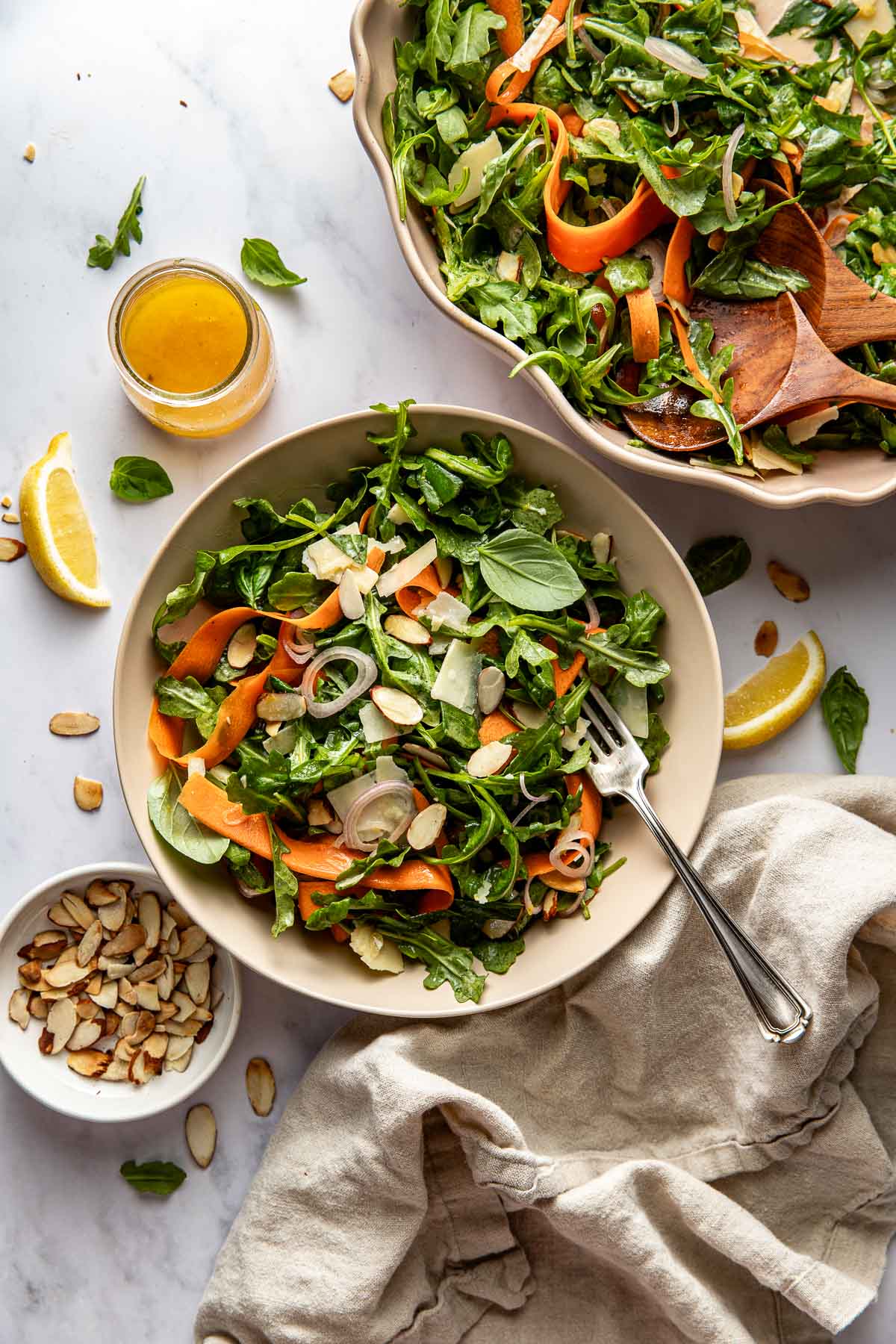 Overhead view of two bowls of colorful Arugula Salad With Lemon And Basil topped with toasted almonds and shaved parmesan cheese. 