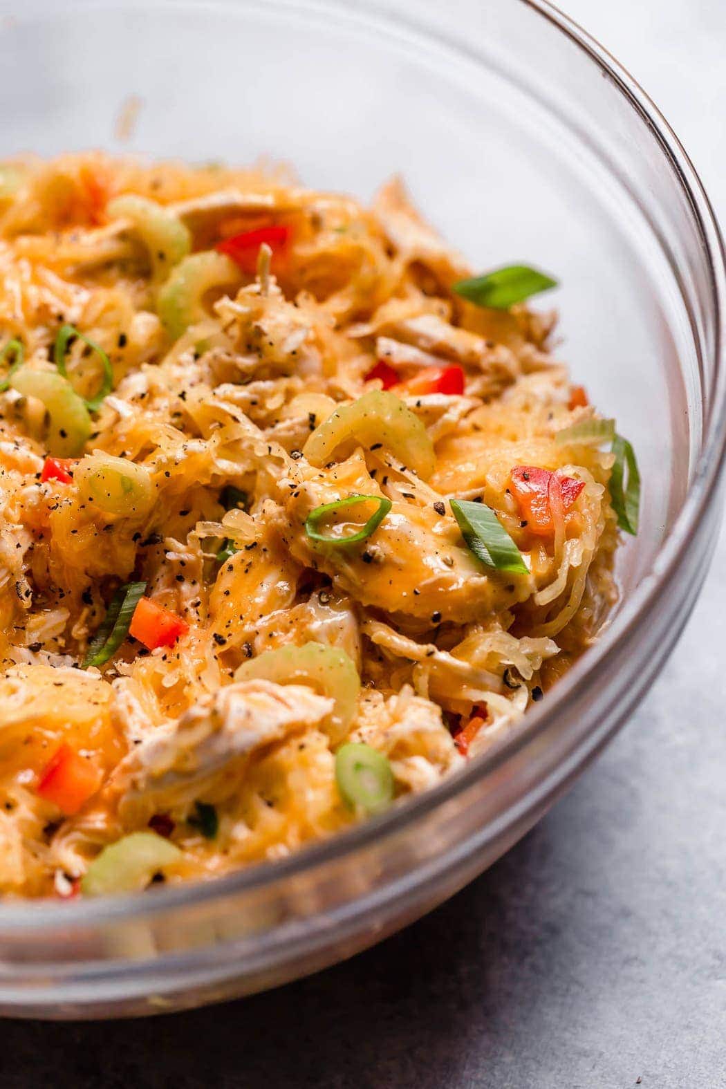 Buffalo chicken and spaghetti squash with red pepper and scallions stirred together in a mixing bowl.