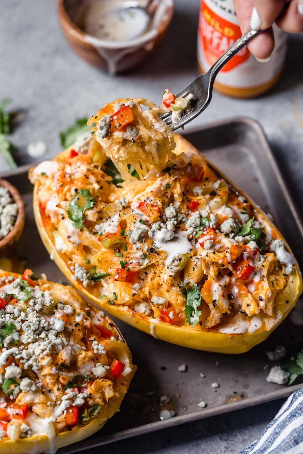 Buffalo Chicken Stuffed Spaghetti Squash in two squash halves topped with blue cheese crumbles, ranch dressing, and buffalo sauce.