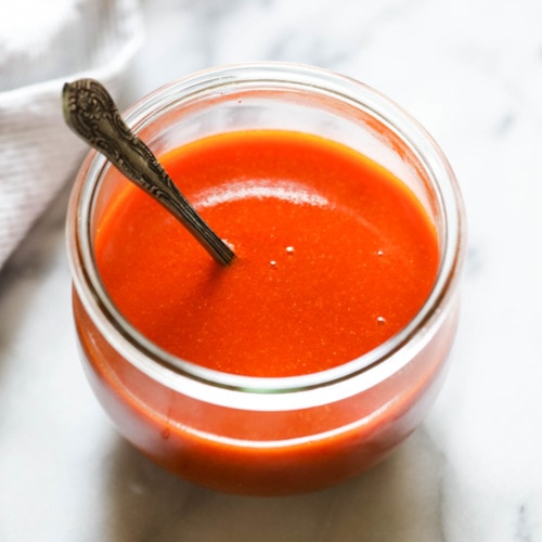 Easy homemade buffalo sauce in a short jar with a spoon in the sauce