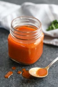 Homemade Buffalo Sauce in a glass bottle with a spoonful resting on the counter