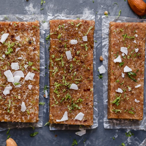 Three key lime energy bars lined up and topped with lime zest and coconut shreds