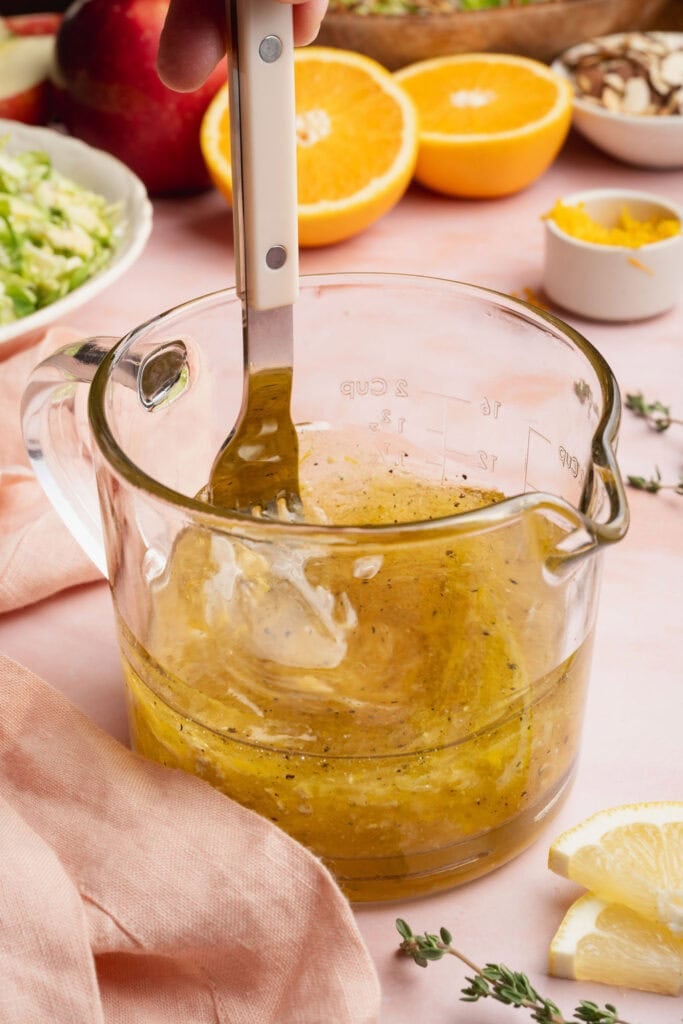 A fork whisking citrus vinaigrette in a glass measuring cup.