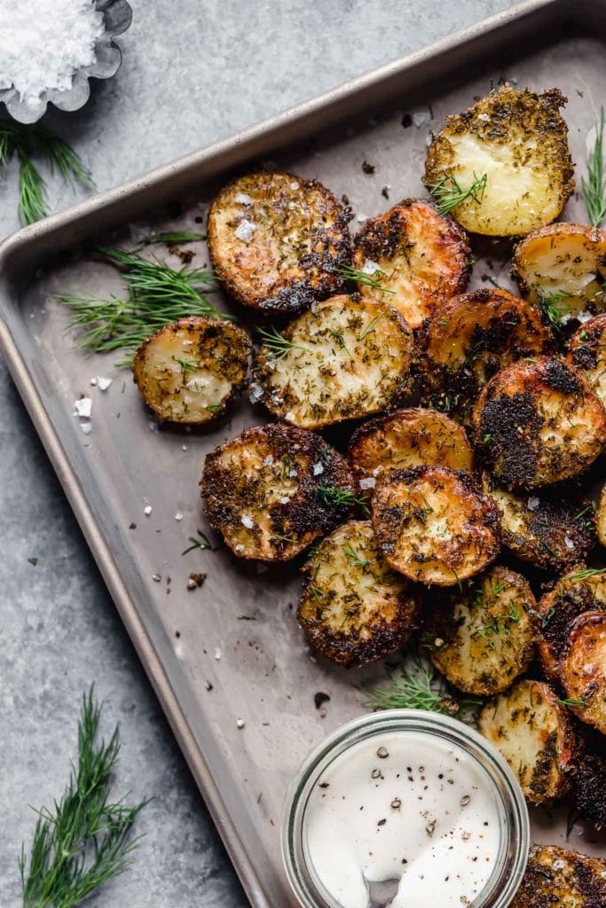Crispy roasted potatoes on parchment-lined baking sheet sprinkled with fresh herbs and sea salt