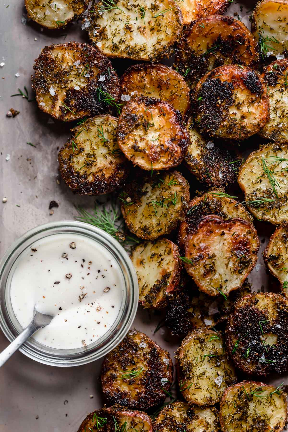 Overhead view Crispy Garlic Ranch Roasted Potato halves on parchment paper, ranch dressing on side.