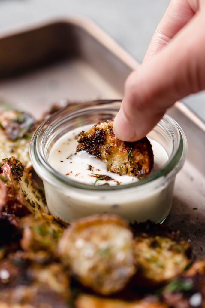 A crispy roasted potato halve being dipped into a small jar of ranch dressing.