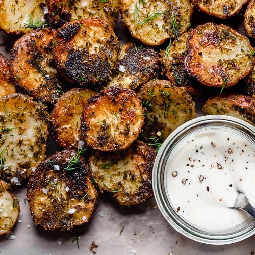 Crispy roasted potatoes on baking sheet sprinkled with sea salt and fresh herbs.