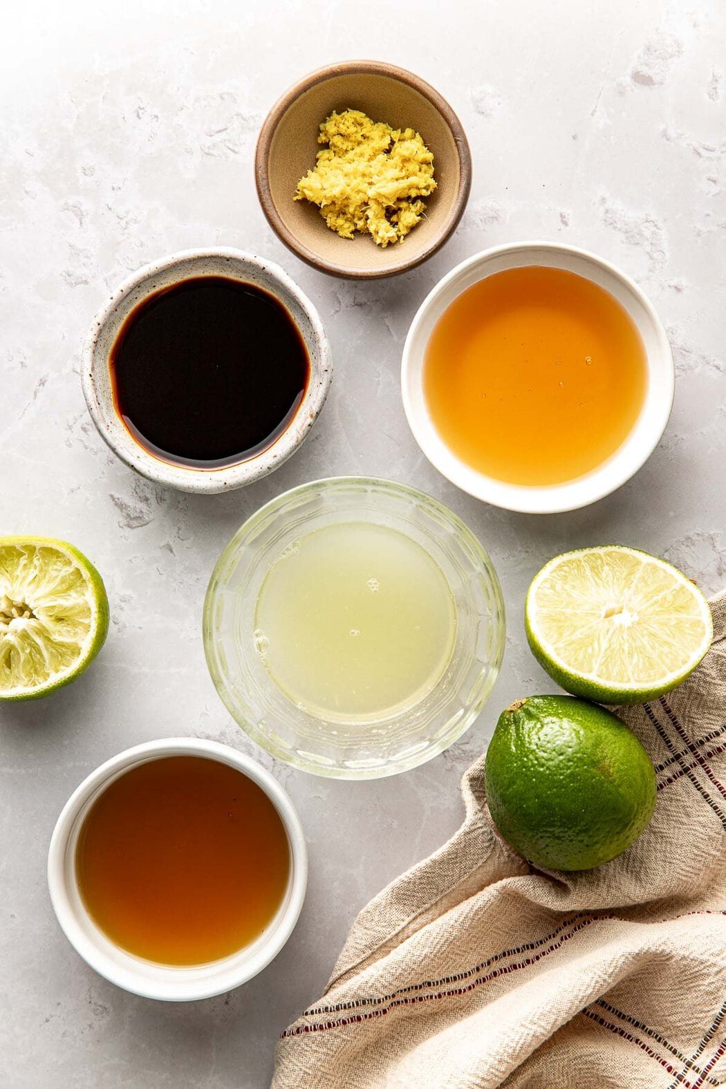 Overhead view of a variety of ingredients for Sesame Ginger Dressing in different sized bowls with sliced limes around the bowls.