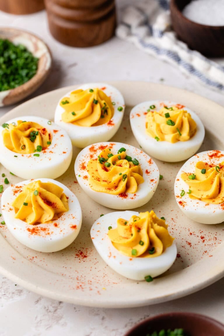 Close up view of a plate of deviled eggs, topped with paprika and fresh chives.