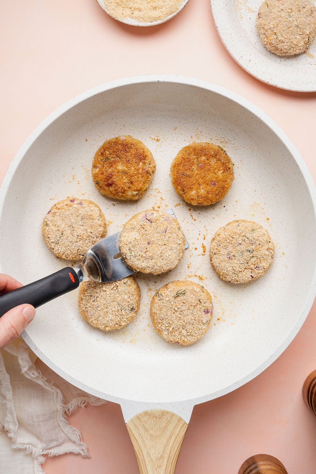 Seven tuna patties cooking in a skillet, two flipped showing a brown side and one being flipped.