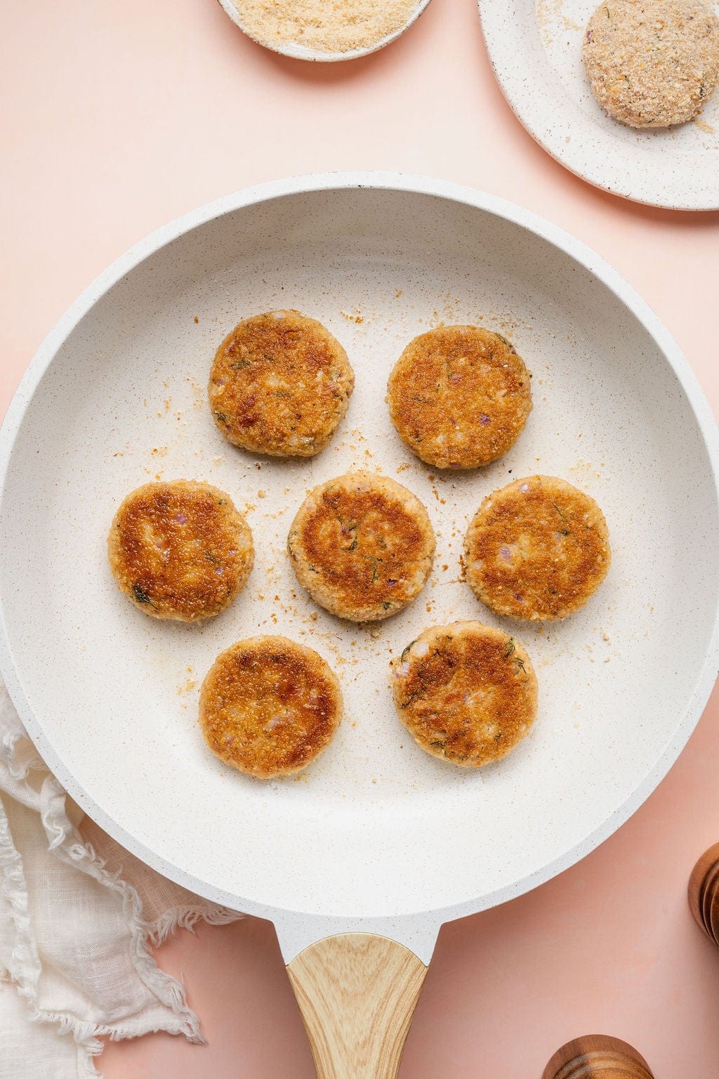 Seven browned tuna patties cooking in a skillet.