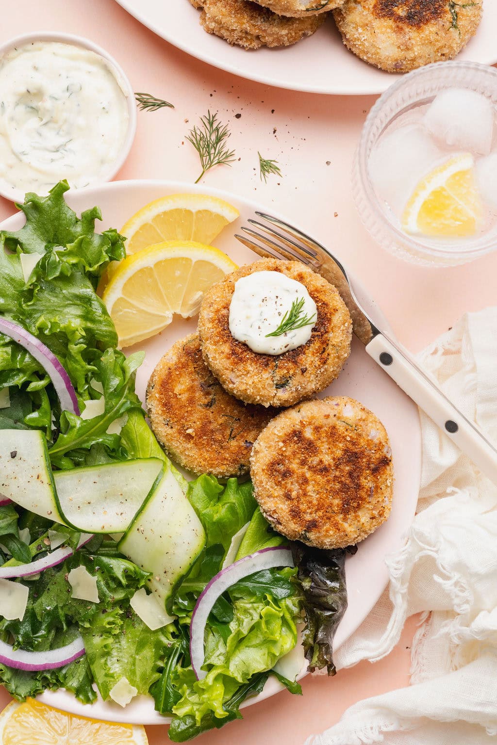 A plate with a green salad, two lemon slices, and three tuna patties, one topped with a dollop of lemon aioli.