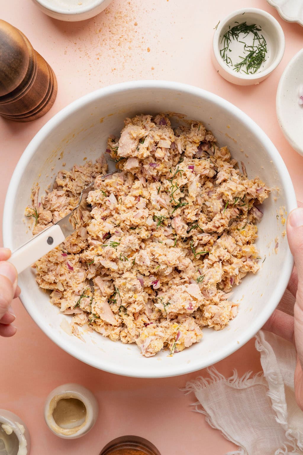 A woman stirring ingredients for tuna patties in a white bowl.