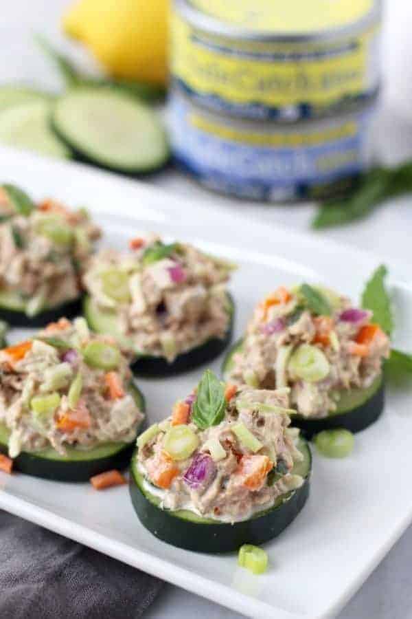 Cashew Tuna Salad Cucumber Bites on a white plate with cans of tuna in the background