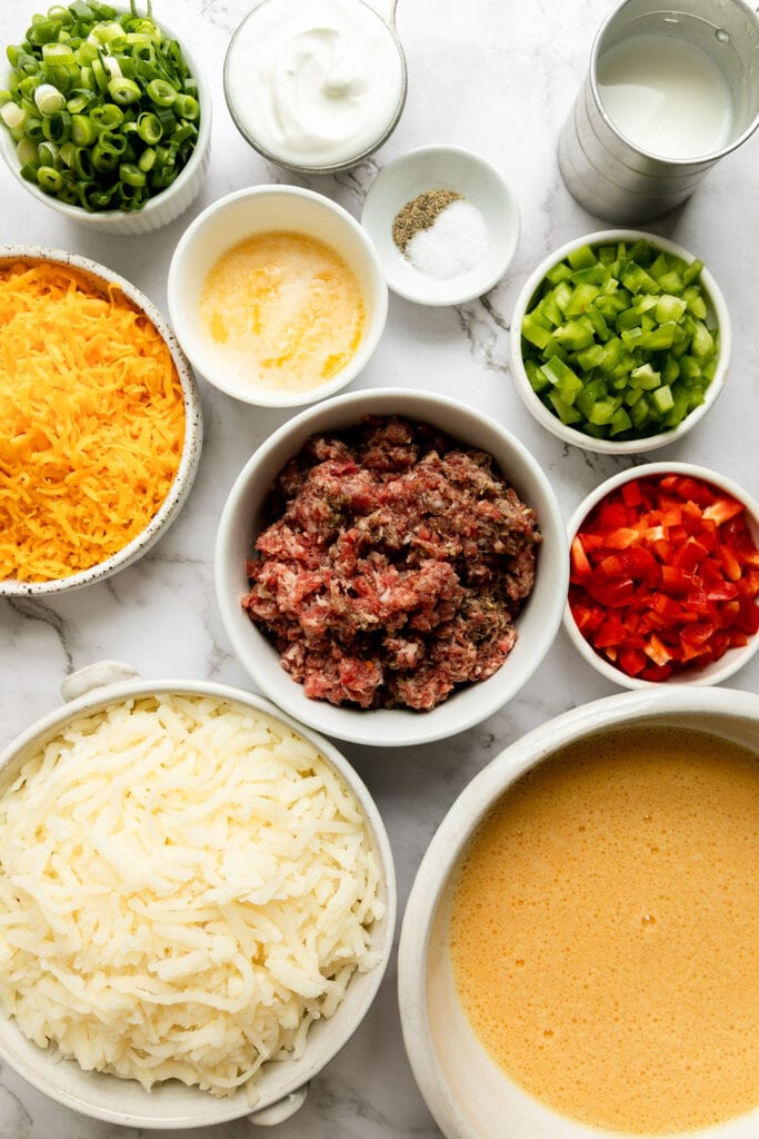 Overhead view of all ingredients for Sausage Egg Bake with Hash browns, arranged together in small bowls. 