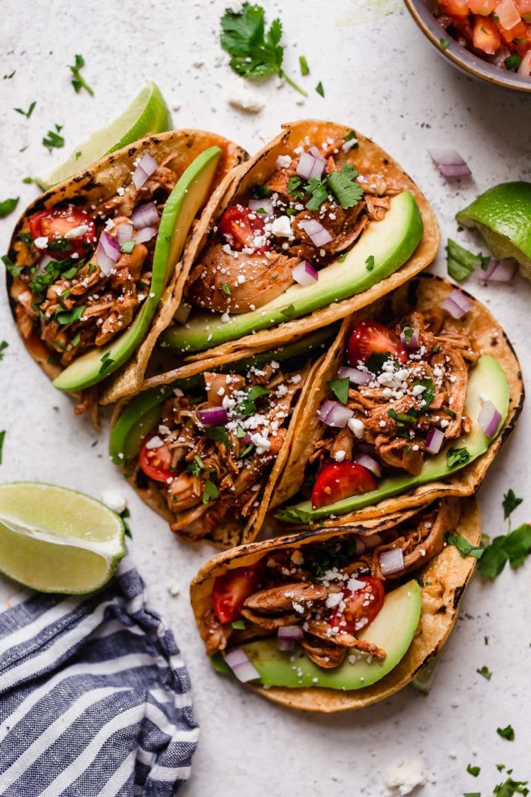 Instant pot shredded chicken tacos in corn shells topped with cilantro and avocado slices.