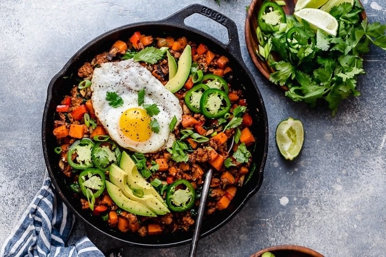 Black Cast Iron skillet filled with sweet potato hash and topped with a fried egg. 