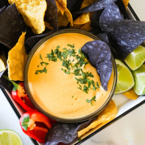 Creamy vegan nacho cheese in a small bowl surrounded with blue and yellow tortilla chips