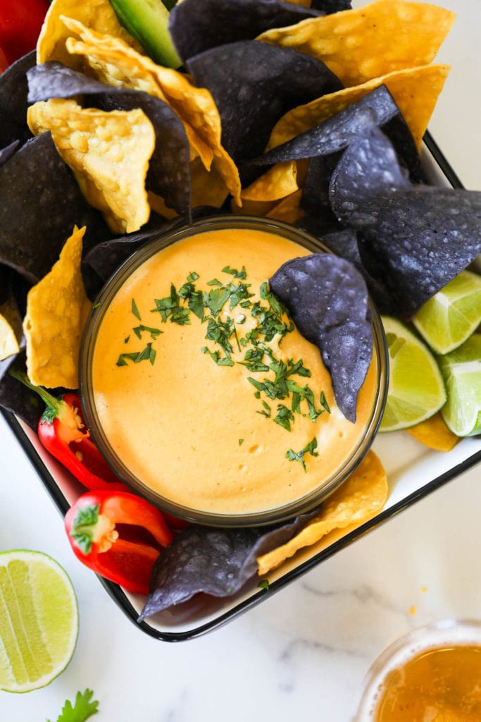 Vegan nacho cheese in a bowl sprinkled with fresh herbs surrounded with blue and yellow tortilla chips