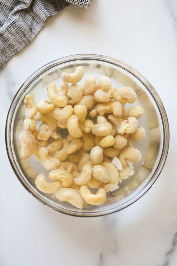 Raw cashews soaking in a bowl of hot water
