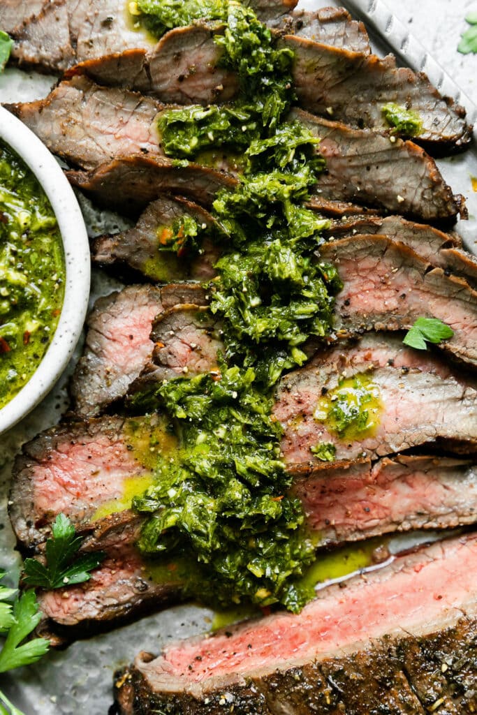 Close up overhead view grilled flank steak with chimichurri sauce spread over stop of cut strips. 