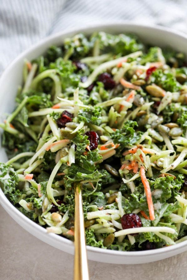 A gold fork filled with creamy broccoli slaw with added kale and dried cranberries ready to be eaten.