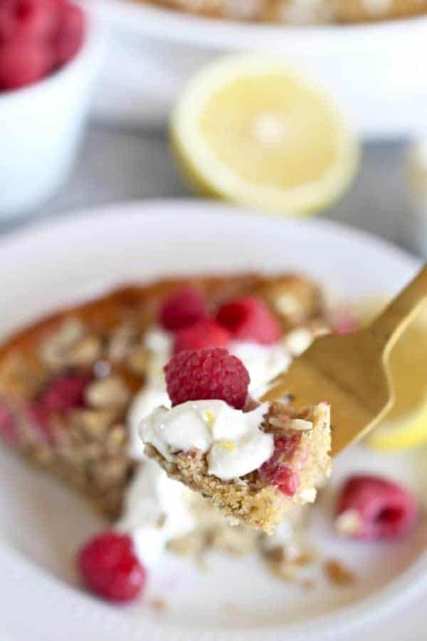 Gluten-free Raspberry Lemon Coffee Cake on a white plate with a bite on a gold fork lifted toward the camera