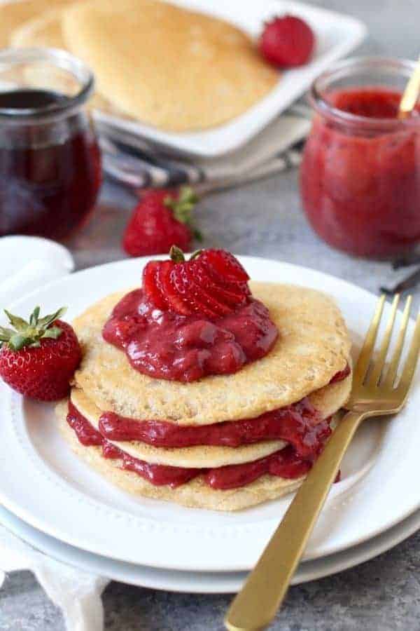 Paleo Vegan Pancakes on a white plate with strawberry jam and strawberries on top