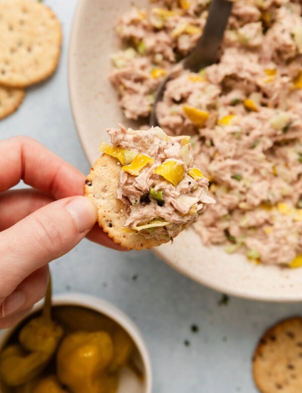 Tuna salad on a cracker, being held above the serving bowl